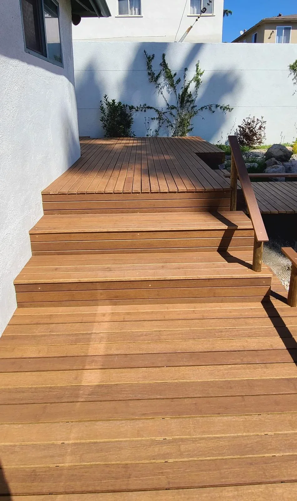 Multi-level composite deck with wooden stairs and handrail in sunny backyard