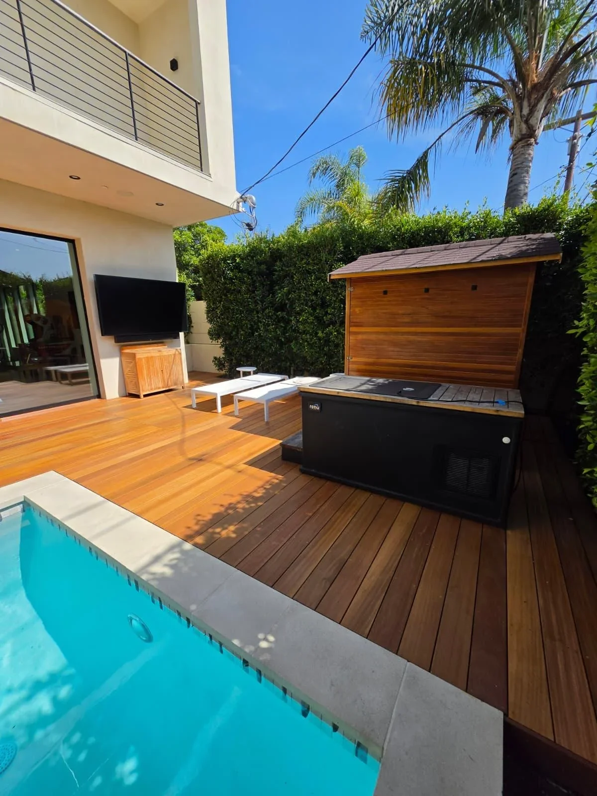 Wooden deck with pool, storage shed, and outdoor entertainment area in sunny backyard
