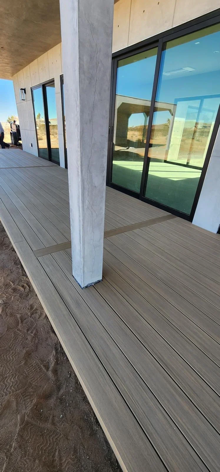 Gray composite deck with black-framed glass doors and concrete column overlooking desert landscape