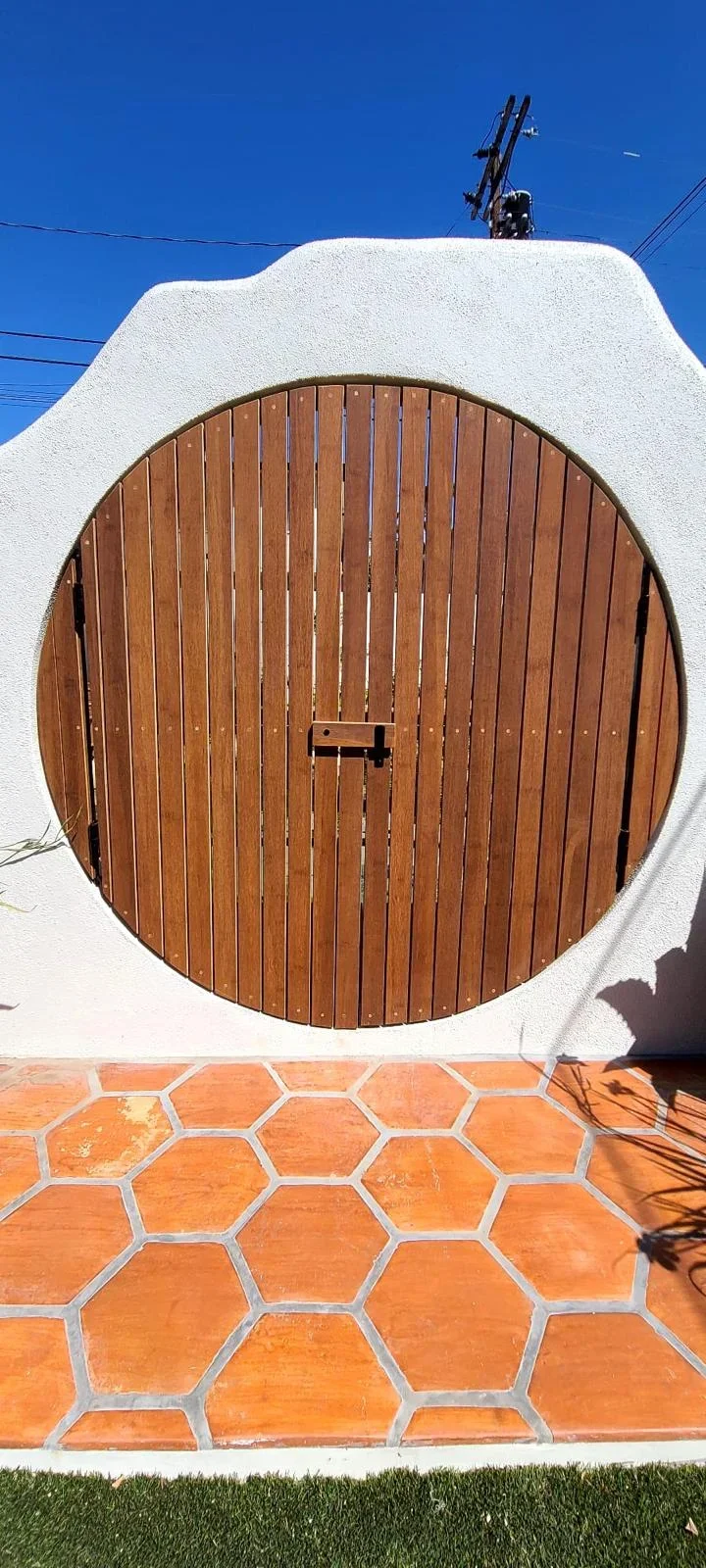 Circular wooden gate with vertical slats in white stucco wall with terracotta tile floor