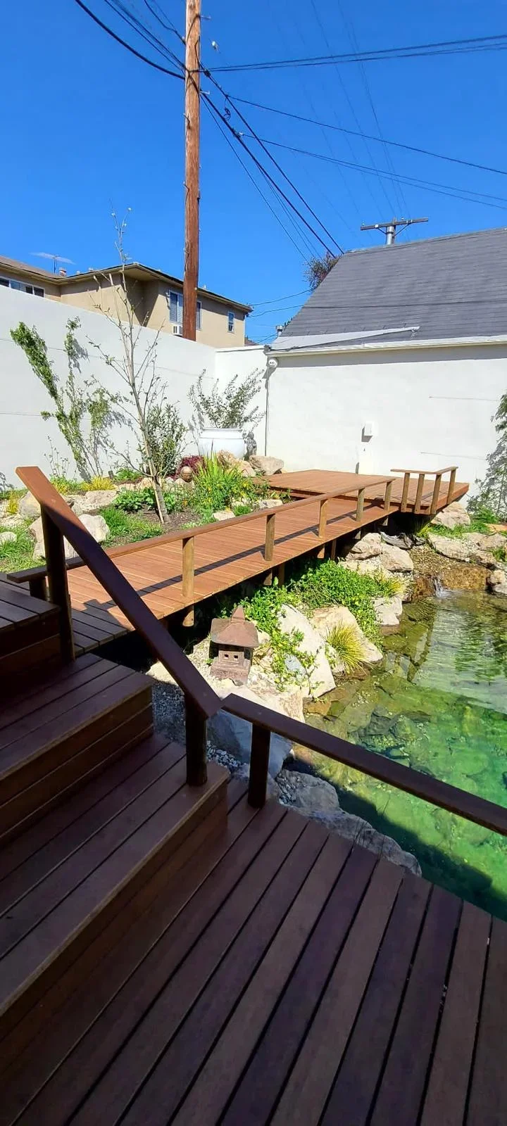 Wooden deck and bridge crossing water feature with dark railings and landscaping
